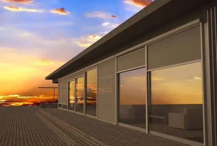 Screens déroulés devant les baies vitrées d’une maison au coucher du soleil