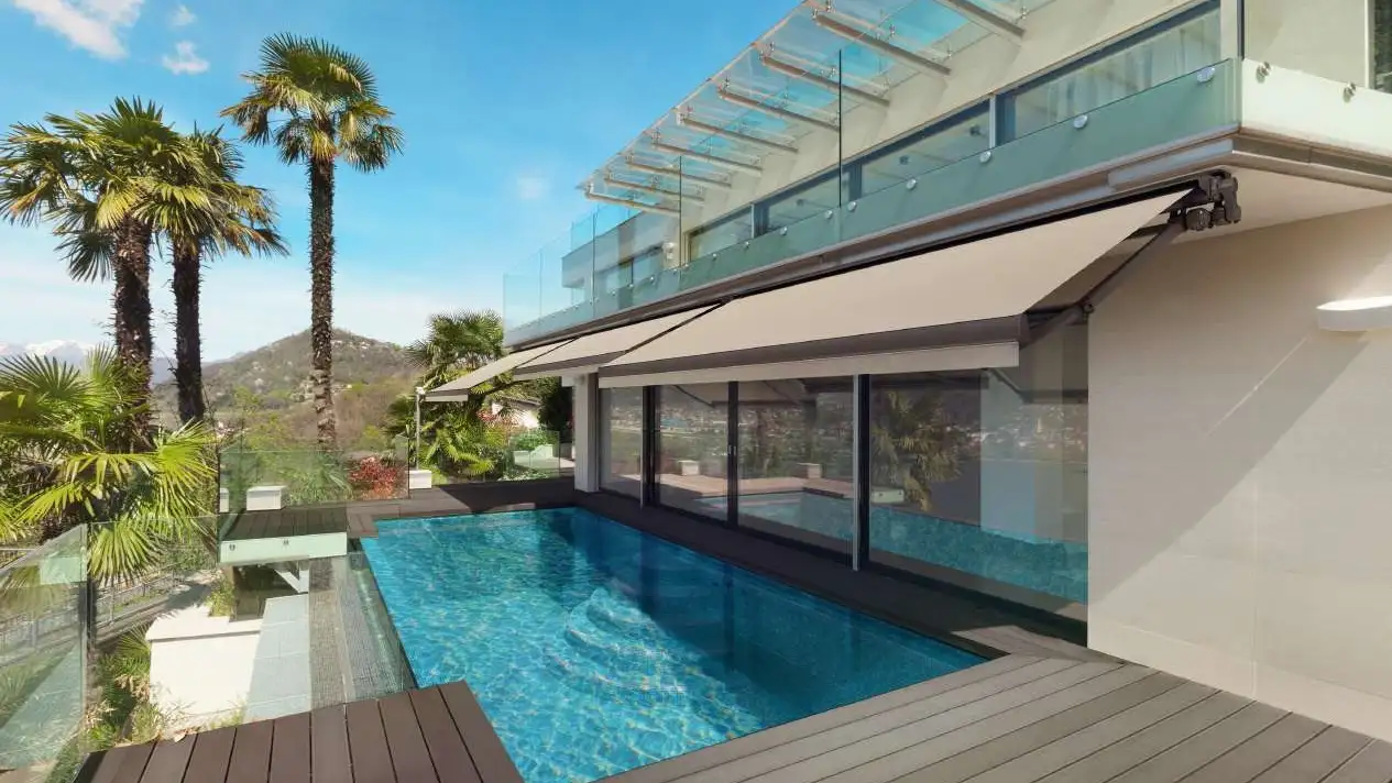 Store banne cassette Design 320 déployé au-dessus d’une terrasse avec piscine et palmiers