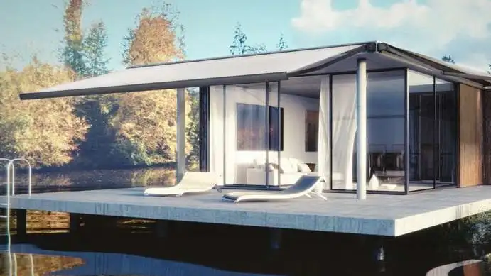 Store banne coffre Excelum 450 de grande largeur déployé devant un pavillon vitré au bord de l’eau