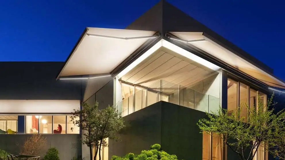 Grand store banne monobloc Design 110 déployé sur une maison contemporaine éclairée à la tombée de la nuit