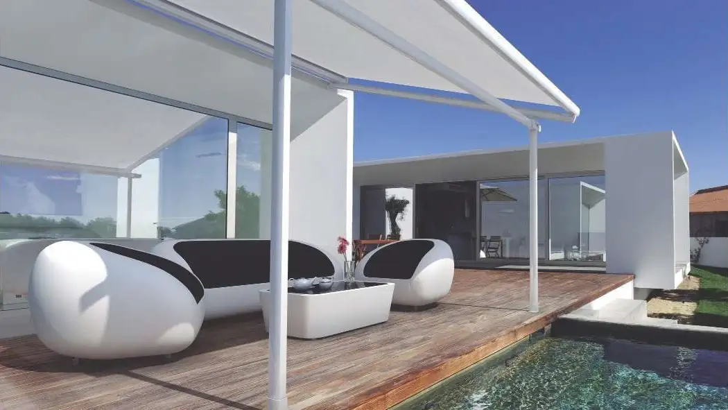 Store de véranda Velysun tendu sous une structure, au-dessus d’un salon extérieur au bord d’une piscine